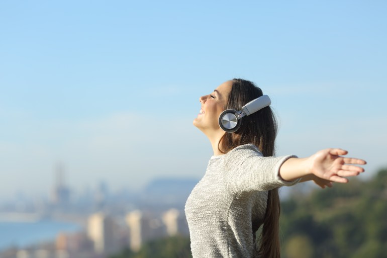 shutterstock_1653533617-1705599058 Girl listening to music with headphones breathing with wide open arms feeling free outdoors