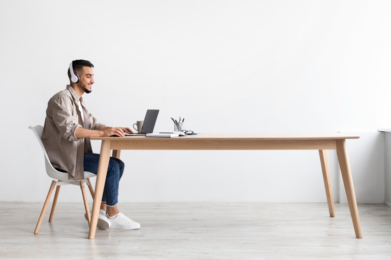 ss2142805773 Cheerful Middle Eastern Freelancer Man Working On Pc Online At Home Listening To Music With Wireless Headphones, Making Research For New Project, Sitting At Desk Enjoying Remote Job, Profile Side View SS2142805773