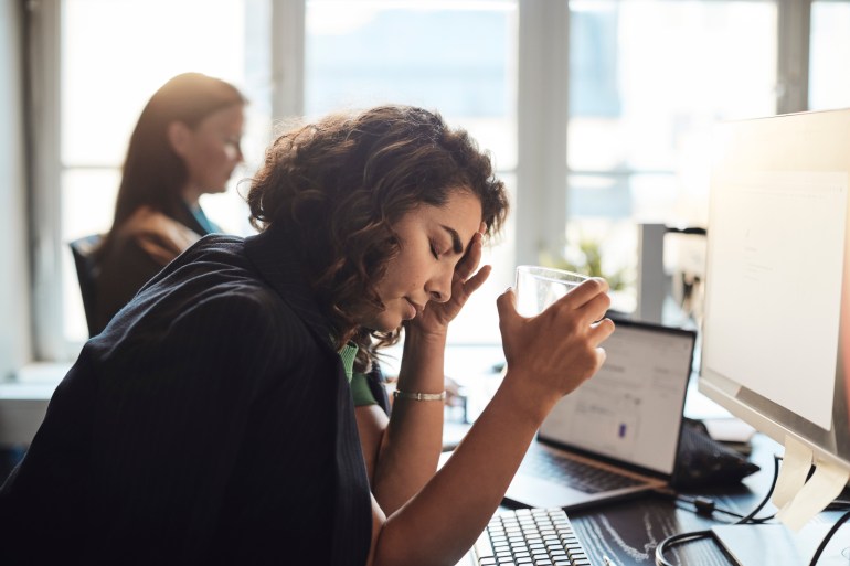 gettyimages-1461604819-1706896663 Tired businesswoman with head in hand holding drinking glass at office