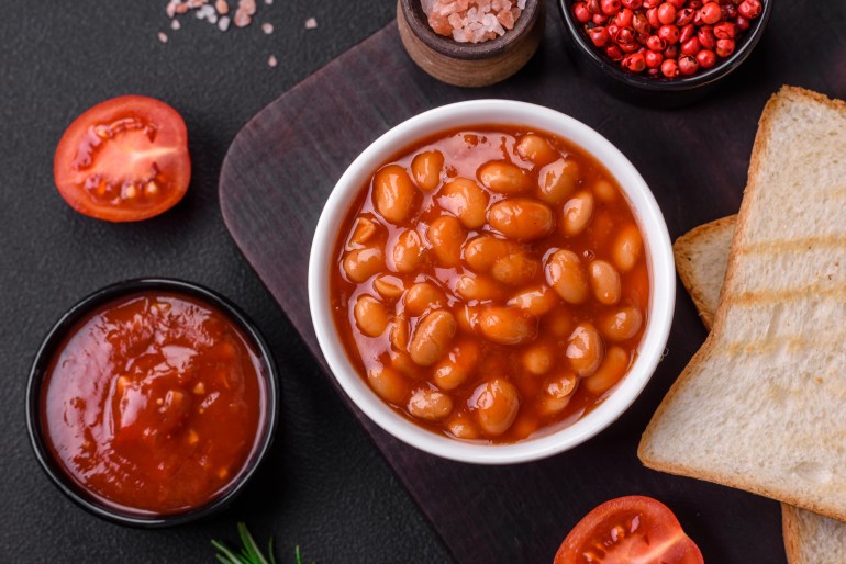 shutterstock_2279406915-1708706520 Delicious canned beans in a tomato in a white ceramic bowl on a dark concrete background