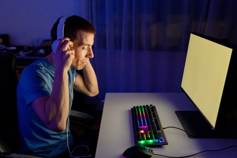 rfdcf-1705825998 One mid adult man play computer video game in dark room, use neon colored rgb mechanical keyboard