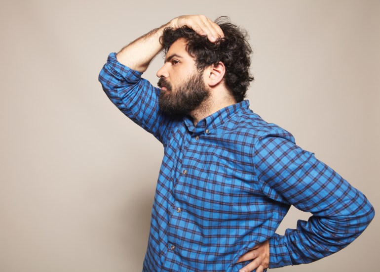 gettyimages-185181123-1713291190 blue chequered shirt, hairy big man, feminine pose, hand on hip, hand on head, black curly hair, beard, beige background, studio lit, fashion