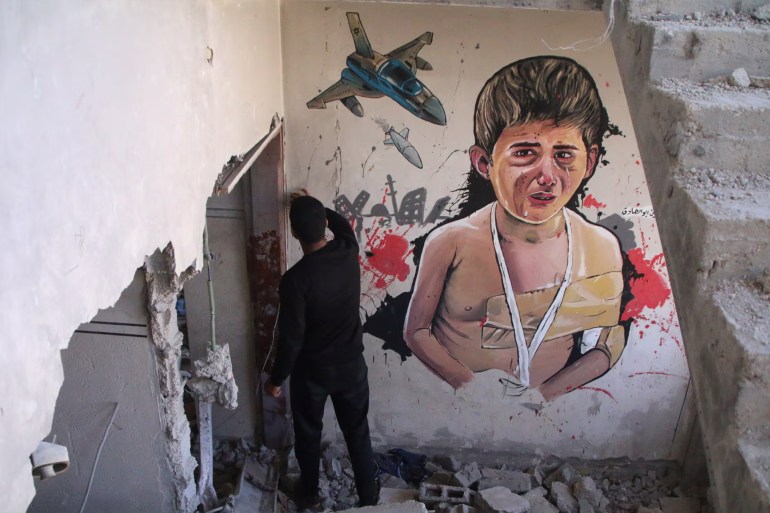 3456-1715085400 رجل فلسطيني يقف بجانب لوحة جدارية مرسومة على منزل مدمر في دير البلح، غزة. صورة فوتوغرافية (غيتي إيمجز)