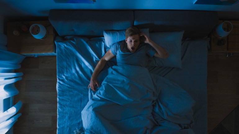 shutterstock_1427499947-1714748922 Top View of a Young Man in Bed at Night Having Terrible Nightmare, He Wakes Up Scared and Covered in Sweat.