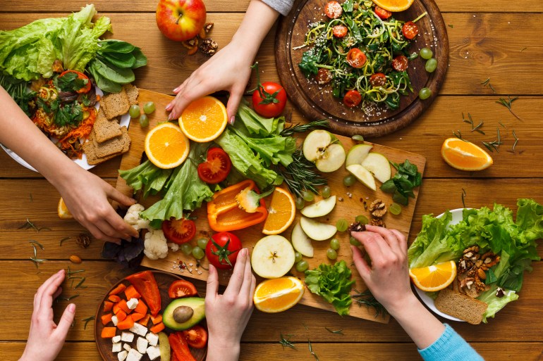 shutterstock_640258210-1715681666 Healthy food dinner table. Women at home together, eating fruits and vegetables, top view, flat lay, crop