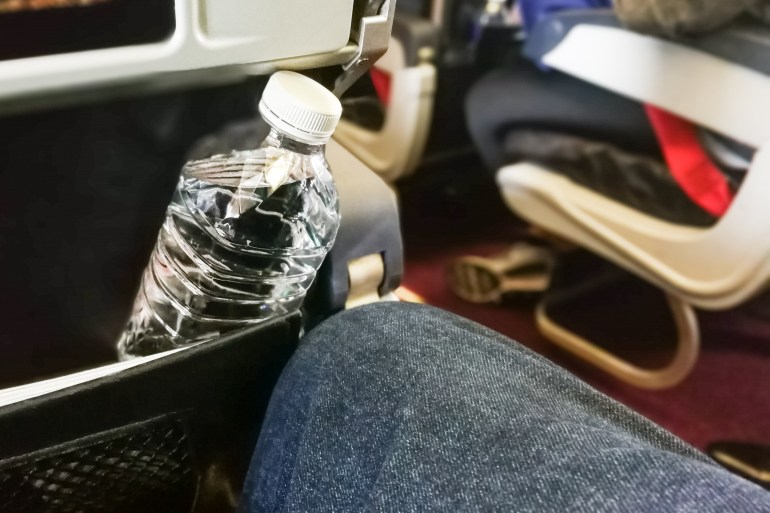 d8b3d8a8d8a8d98ad8a82-1717505504 Passenger holding mineral water bottle in aeroplane cabin. Advice to drink lots of water to keep oneself hydrated on long haul flight.