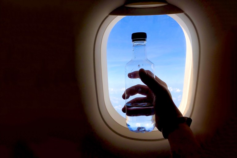 d8b3d8a8d8a8d98ad8a83-1717505512 hand holding water bottle near airplane window; Shutterstock ID 1627184908; purchase_order: aljazeera ; job: ; client: ; other: