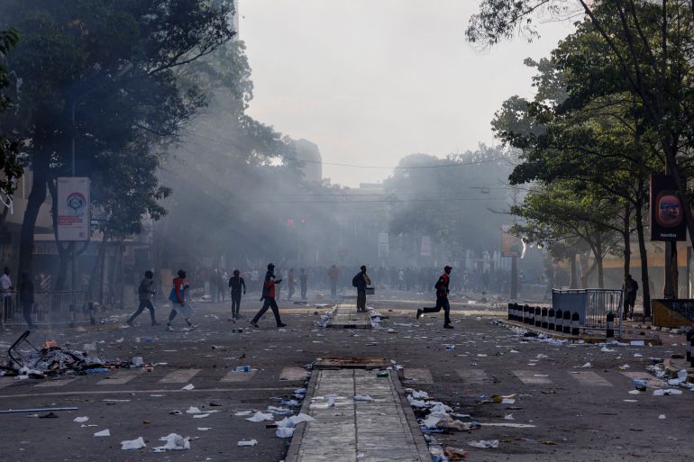 People cross a street with strewn debris in the aftermath of clashes between protesters and riot police near Parliament buildings during a nationwide strike to protest against tax hikes and the Finance Bill 2024 in downtown Nairobi, on June 25, 2024. Kenyan President William Ruto vowed to take a tough line against "violence and anarchy" on June 25, after protests against his government's proposed tax hikes turned deadly and demonstrators ransacked parliament. Mainly youth-led demonstrations had been largely peaceful as they grew over the past week but chaos erupted in Nairobi on June 25, with crowds throwing stones at police, pushing past barricades and entering the grounds of parliament. (Photo by Tony KARUMBA / AFP)