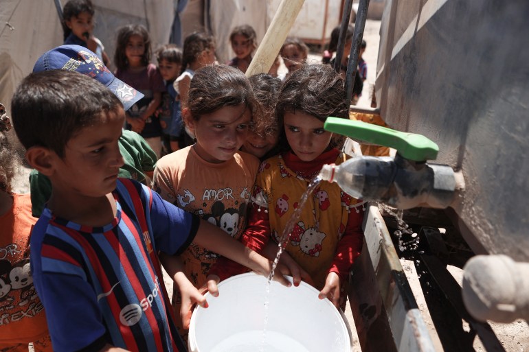 Syrian children fill their buckets with water at a camp for internally displaced people (IDP) near Sarmada, in the northern Syrian province Idlib on June 28, 2024. - After 13 years of civil conflict, lack of international funding has severely undercut the provision of basic services such as water, waste disposal and sanitation in displacement camps in northwest Syria, according to the United Nations. More than five million people, most of them displaced, live in areas outside government control in Syria's north and northwest, according to the UN, many relying on aid to survive. (Photo by AAREF WATAD / AFP)
