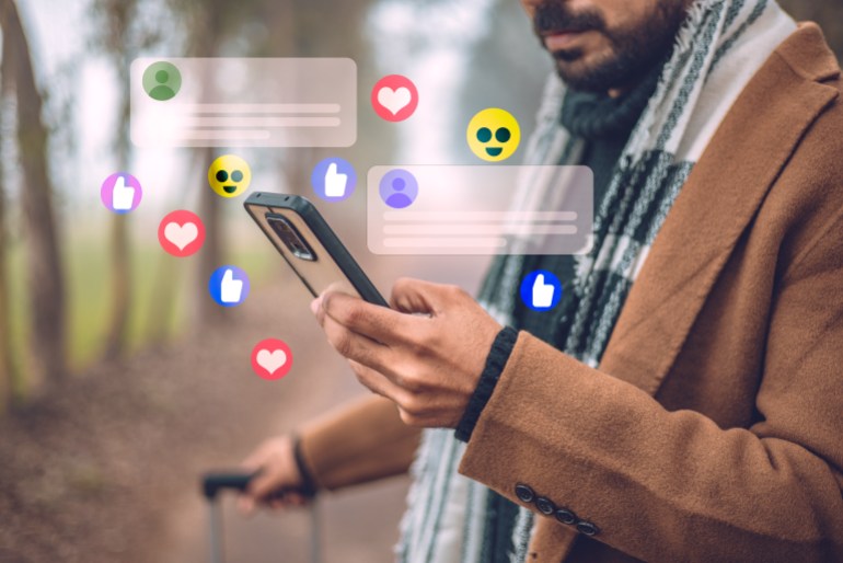gettyimages-1904838938-1721229352 While traveling, a handsome man uses his smartphone to stay connected to social media, receiving notifications and commenting on posts.