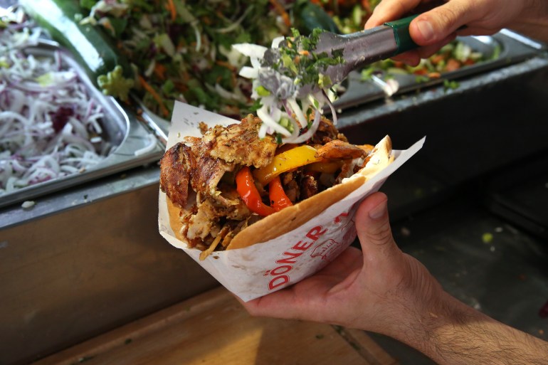 1407116566-1723118147 BERLIN, GERMANY - JULY 06: An employee prepares a customer's order at Mustafas Gemüse Kebap on July 06, 2022 in Berlin, Germany. The döner kebab, a fast food sandwich made of stacked, seasoned meat turned on a rotisserie, was popularized in Germany in the early 1970s by Turkish guest workers (Gastarbeiter in German, or migrants arriving in Germany after World War II to counter labor shortages), with more stands offering the dish in Berlin than in Istanbul, and many considering it to be Germany's national dish. (Photo by Adam Berry/Getty Images)