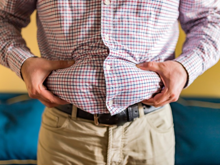 159f5728-e8c2-4bc3-9766-8994a527090f Midsection Of Man Holding Belly Fat At Home، كرش، بطن، بدانة، دهون، سمنة، زيادة الوزن، وزن، ميزان شحوم