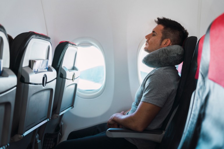gettyimages-1092344546-1723219022 Man sleeping with neck pillow in airplane