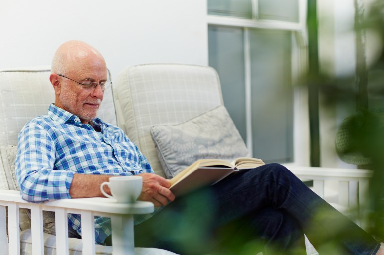 gettyimages-492275647-1722772293 Senior man reading book while relaxing on chair at porch