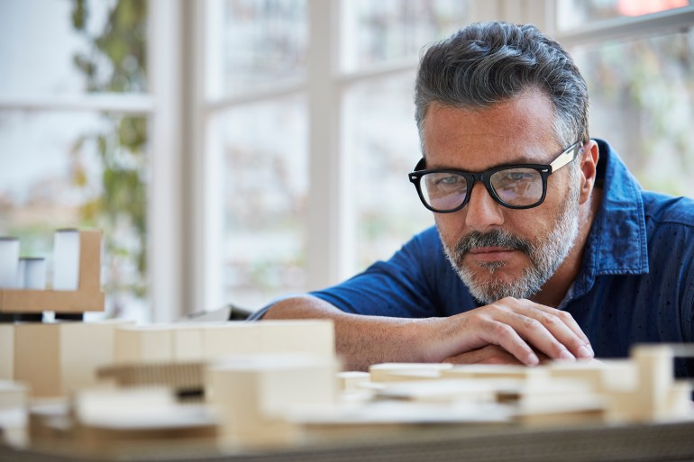gettyimages-589090443-1722796443 Mature male architect looking at building model in office