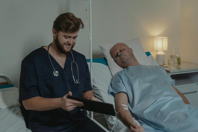 Man Wearing a Blue Scrub Suit Sitting beside a Patient