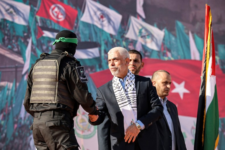 Yahia al-Sinwar (C), Gaza Strip chief of the Palestinian Islamist Hamas movement, shakes hands with a masked fighter of Hamas' Qassam Brigades during a rally marking the 35th anniversary of the group's foundation, in Gaza City on December 14, 2022. Hamas will end talks on securing a prisoner exchange with Israel unless there is progress soon, the militant group's leader in the Gaza Strip said on December 14. Since Israel's 2014 invasion of the Gaza Strip, the Islamist group has held the bodies of Israeli soldiers Oron Shaul and Hadar Goldin, although Hamas has never confirmed their deaths. Earlier this year Hamas published a video of an Israeli civilian detained for seven years in the enclave. (Photo by MOHAMMED ABED / AFP)
