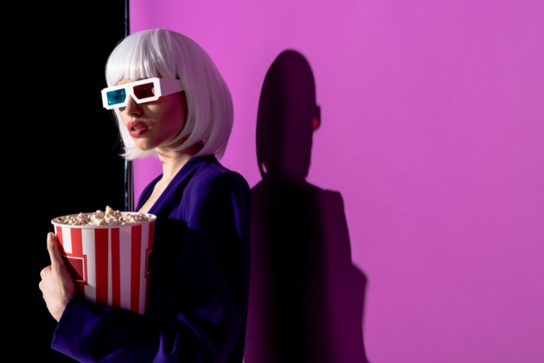 movie3-1727362264 Interested girl in 3d glasses holding popcorn on purple background