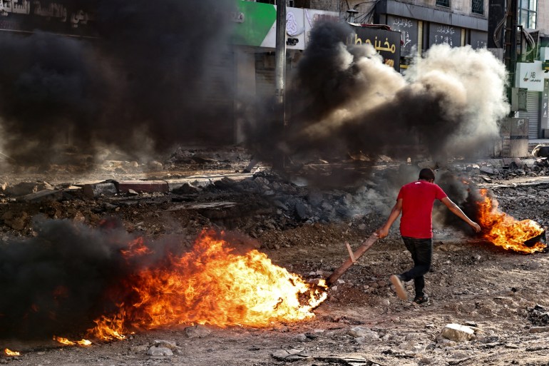 A Palestinian runs past tyres set ablaze by youths in Jenin in the occupied West Bank on September 4, 2024, during an ongoing Israeli military raid. - Israeli forces have killed at least 30 Palestinians across the northern West Bank since August 28, the territory's health ministry says, while Israel's military reported one soldier killed in the "counter-terrorism" raids. (Photo by Zain JAAFAR / AFP)