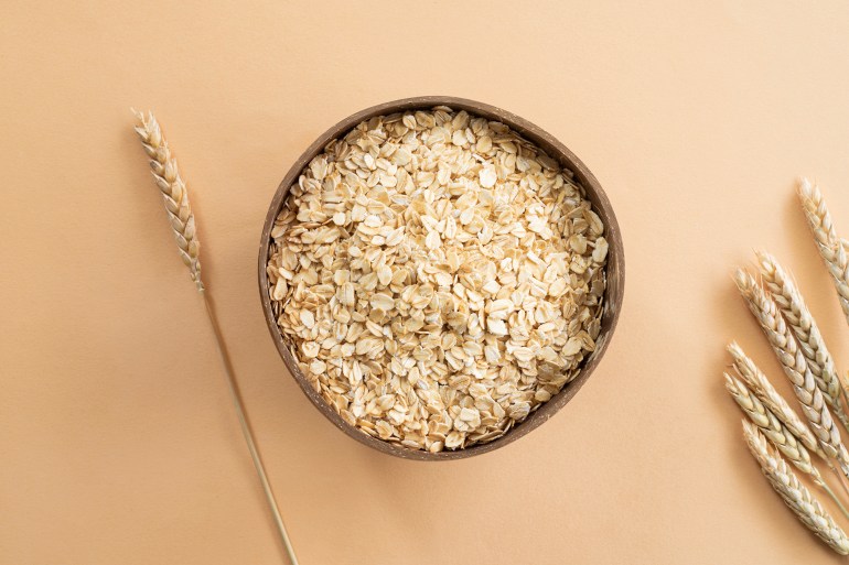 shutterstock_2427948055-1727013777 Oats or oat flakes in wooden bowl and golden wheat ears on beige background. Top view, horizontal. Healthy lifestyle, healthy nutrition, vegan food concept; Shutterstock ID 2427948055; purchase_order: aj net; job: ; client: ; other: