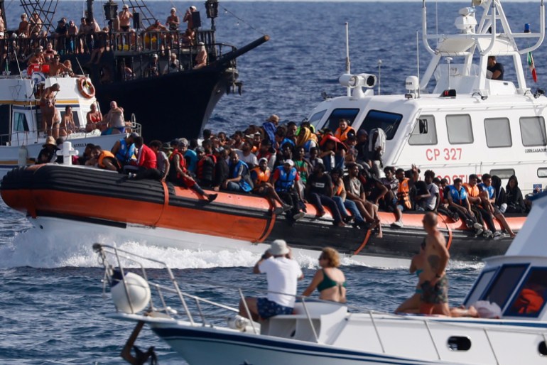 2-photo-1695467121 An Italian Coast Guard boat carries migrants as tourists on boat, foreground, watch, near the port of the Sicilian island of Lampedusa, southern Italy, Monday, Sept. 18, 2023. (Cecilia Fabiano/LaPresse via AP)