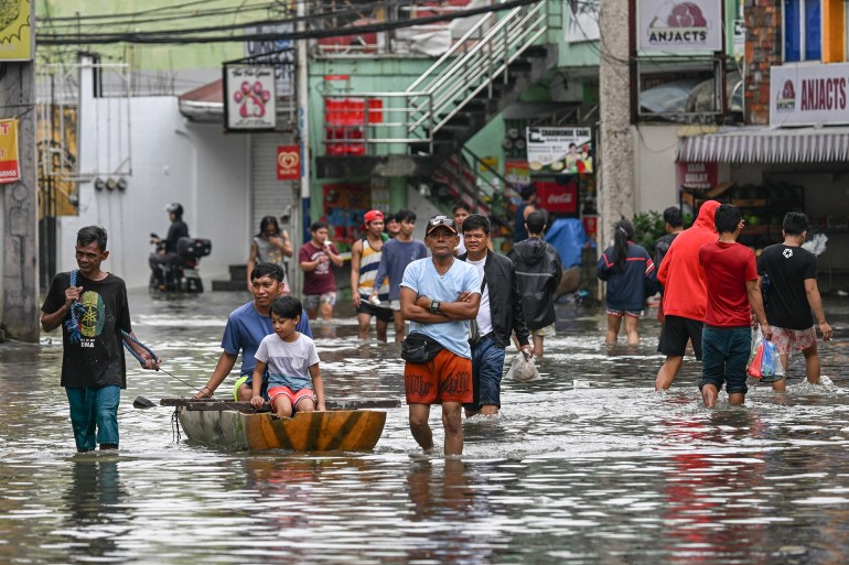 People wade through a street that was flooded by heavy rains brought about by Tropical Storm Trami in Cainta, Rizal province, East of Manila, on October 25, 2024. - Philippine rescue workers battled floodwaters on October 25 to reach residents still trapped on the roofs of their homes as Tropical Storm Trami moved out to sea after killing at least 40 people. (Photo by JAM STA ROSA / AFP)