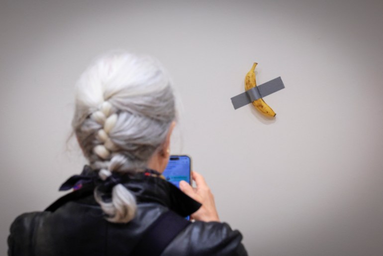 85-1732171604 (FILES) A journalist takes a picture of Italian visual artist Maurizio Cattelan's duct-taped Banana entitled "Comedian," displayed during a media preview at Sotheby's in New York, on November 8, 2024. - A fresh banana taped to a wall -- a provocative work of conceptual art by Italian artist Maurizio Cattelan -- was bought for $6.2 million on November 20, 2024 by a cryptocurrency entrepreneur at a New York auction, Sotheby's announced in a statement. The debut of the edible creation entitled "Comedian" at the Art Basel show in Miami Beach in 2019 sparked controversy and raised questions about whether it should be considered art -- Cattelan's stated aim. (Photo by kena betancur / AFP) / RESTRICTED TO EDITORIAL USE - MANDATORY MENTION OF THE ARTIST UPON PUBLICATION - TO ILLUSTRATE THE EVENT AS SPECIFIED IN THE CAPTION / TO GO WITH AFP STORY BY Ana FERNANDEZ: "Magritte, Rucha and... a banana, in a bid to set new records at New York auctions"