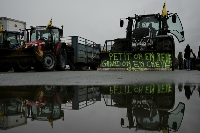 afldemo-1732207674 French farmers members of the "Coordination Rurale" farmers' union (CR) stand next to a tractor with a banner reading "As a child we dream of it as an adult we die of it" as they gather at a logistic hub, in Beychac-et-Caillau, southwestern France on November 20, 2024, on the third day of a nationwide protest against EU-Mercosur agreement. - Farmers complain about excessive bureaucracy and low incomes, but they're also fed up with poor harvests and losses from emerging animal diseases. Farmers also protest against the free-trade agreement between the European Union and the Latin American countries of Mercosur, with Paris leading resistance against ratification of the deal that would create the world's largest free trade zone. (Photo by Philippe LOPEZ / AFP)