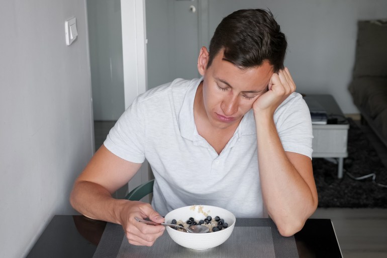 airports5-1732111161 sleepy sunburned man in t-shirt sits at table resting head with hand and eats healthy breakfast at hotel restaurant in morning; Shutterstock ID 1714895911; purchase_order: aljazeera ; job: ; client: ; other: