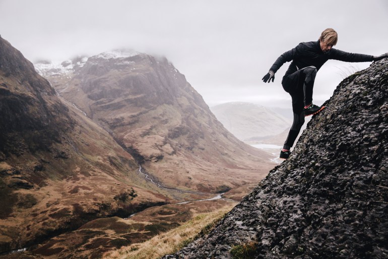 gettyimages-680676715-1732108752 A free runner climbs a steep mountain rock face with the view of the three sisters mountains in the background.