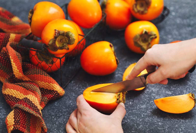 gettyimages-897778624-1731855274 Woman's hands cutting fresh persimmon fruits.