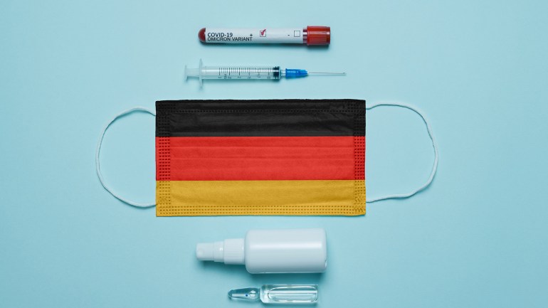 01-2 Blood tube for test detection of virus Covid-19 Omicron Variant with positive result, medicine mask with Germany flag superimposed and vaccine. New Variant of the Covid-19 Omicron