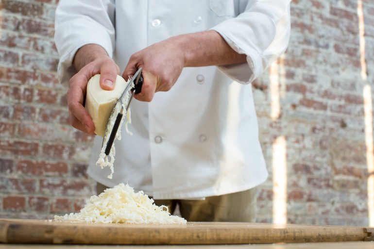 gettyimages-579110457-1733413507 Man Hand Grates Mozzarella