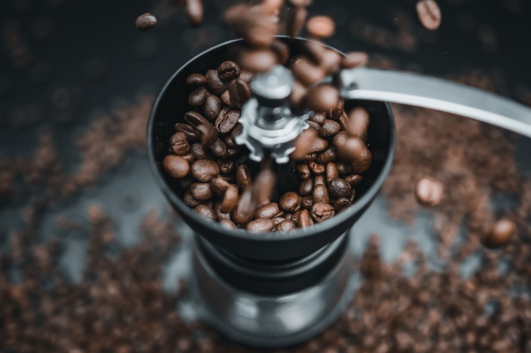 shutterstock_1705697668-1702221978 Fried coffee beans are falling to the manual grinder. Cinematic dark colors. Preparation of fresh beverage morning coffee for breakfast. Mill for grinding. Isolated on black background.