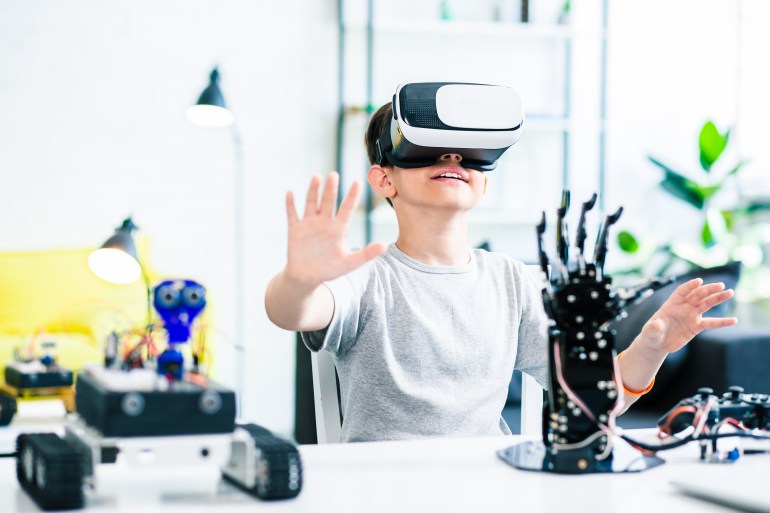 shutterstock_1213293706 Nice smart enthusiastic boy sitting at the table and wearing VR glasses while experimenting with his robotic devices; Shutterstock ID 1213293706; Department: -