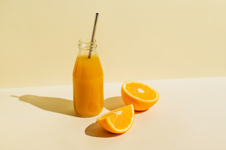gettyimages-1465038961-1739542124 Colorful bottle of freshly squeezed orange juice with fresh ingredients oranges on beige background. Superfoods, healthy food, drinks, diet and detox concept. Flat lay, top view, copy space