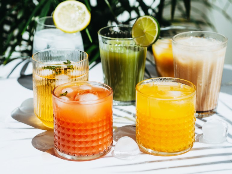 gettyimages-2150712881-1739542166 Various refreshing non-alcoholic drinks in glasses with ice. Different juice, lemonade, iced coffee, kombucha and smoothies on table and green plant background.