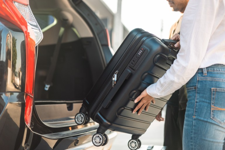 shutterstock_2265213147-1738845721 Happy couple puts his suitcase in the back of the car and prepares to leave for honeymoon trip. Husband and wife open the back of the car put luggage travel. Couple moving into new home at moving day