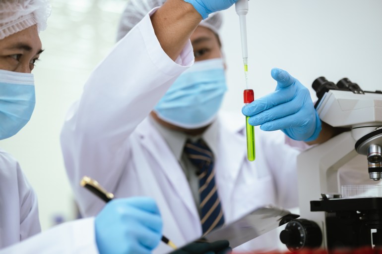 Scientists in a laboratory in Asia are conducting medical tests by analyzing chemical samples under a microscope to advance biotechnology research into disease and stem cells.