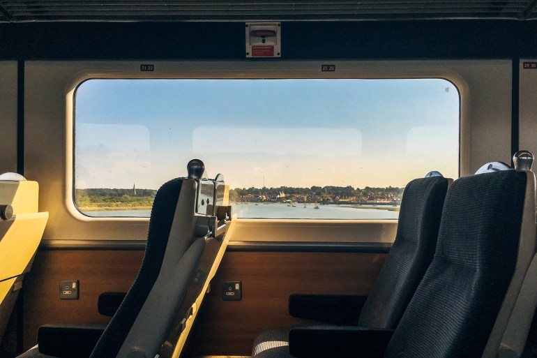 Side view of empty passenger seats in a modern train carriage interior with scenic coastal view out of the window at dusk.