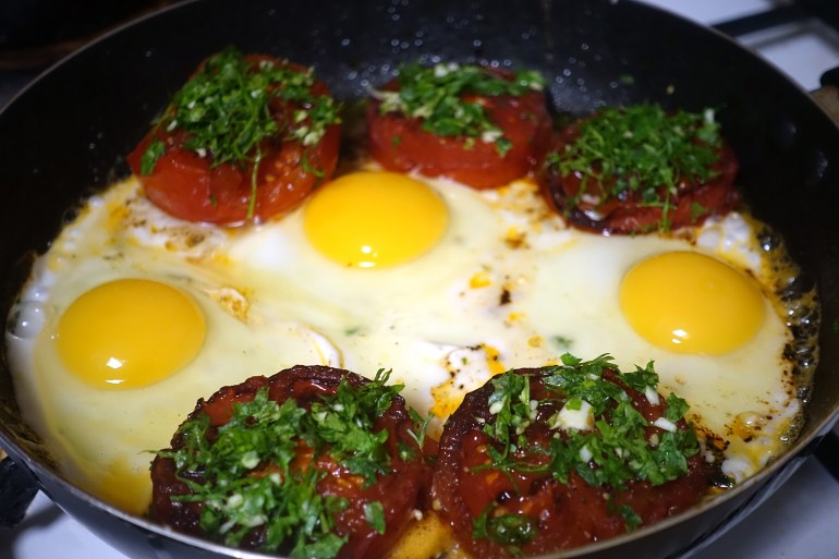Provencal tomatoes with fried eggs being cooked in a frying pan