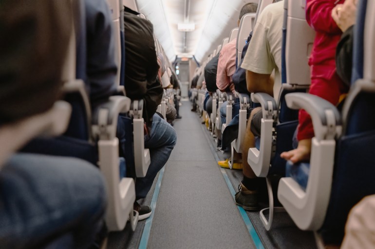 Airplane Aisle with View Of People Sitting on Their Seats - stock photo