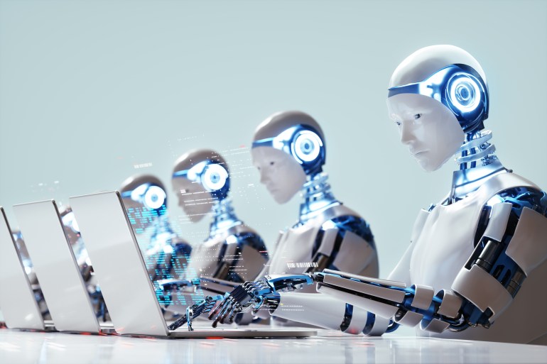 gettyimages-2022302070-1718023682-2 Digital generated image of multiple robots working on laptops siting in a raw. Smart technology, automation and artificial intelligence concept.