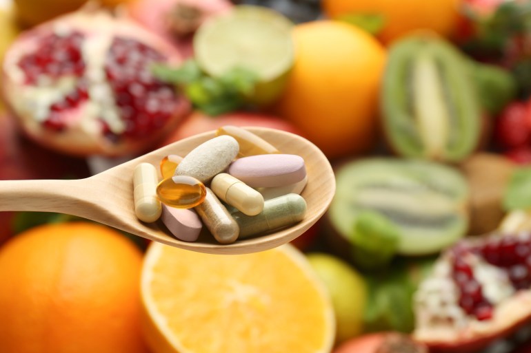 Different vitamin pills in spoon over fresh fruits, closeup. Space for text