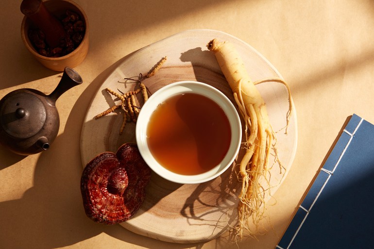 shutterstock_2218536173-1741285316 A bowl of tonic made from ginseng, Ganoderma lucidum, and cordyceps is displayed on a wooden platform. Books, teapots, and mortars of dried herbs on the golden paper background; Shutterstock ID 2218536173; purchase_order: aj; job: ; client: ; other: