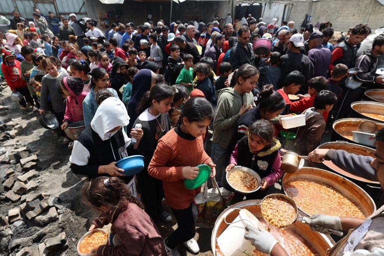 Palestinians wait in front of a free food distribution point to receive their portion of a hot meal, at the Nuseirat refugee camp in the central Gaza Strip on April 12, 2025. On March 2 this year, Israel imposed a full blockade on the Palestinian territory, and cut off power to Gaza's main water desalination plant. (Photo by Eyad BABA / AFP)