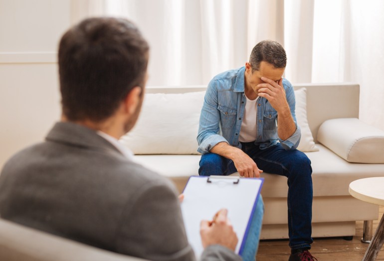 Therapy miracle.Selective focus of mournful tragic male patient looking down and sitting on the couch while psychologist listening to him