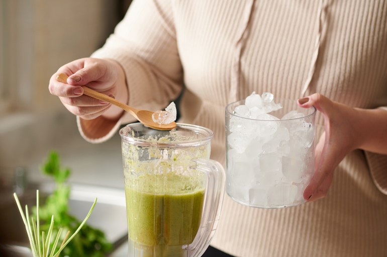 Close-up image of woman adding ice cubes in green smoothie; Shutterstock ID 2163846423; purchase_order: aj; job: ; client: ; other: