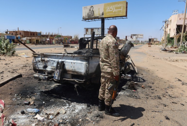 A Sudanese army soldier stands next to a destroyed combat vehicle as Sudan's army retakes ground and some displaced residents return to ravaged capital in the state of Khartoum Sudan March 26, 2025. REUTERS/El Tayeb Siddig