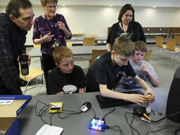ADVANCE FOR USE SUNDAY, JUNE 8 AND THEREAFTER - In this April 11, 2014 photo, Andy Merrill, 13, of Libertyville, Ill., connects a monitor and keyboard to a Raspberry Pi, a credit-card sized computer, during a teen program called "Teen Tinkers and Minecraft" at Cook Park Library in Libertyville. He explains how the computer purchased by the library works to Russ Cerqua, libraries business manager, left to right standing, Ellen Jennings, teen librarian, and Heather Beverley, assistant manager in the children department, along with members of the teen group. (AP Photo/Daily Herald, George LeClaire) MANDATORY CREDIT, MAGS OUT